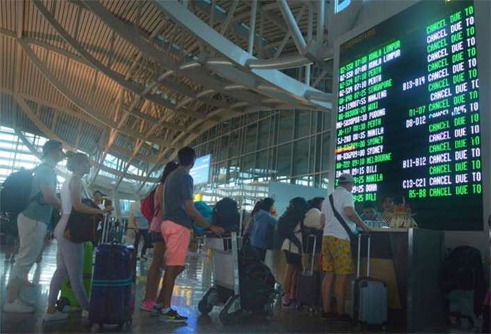 Passengers stand in front of a display board in Denpasar airport after their flights were cancelled