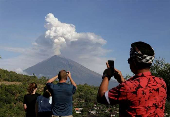 A local guide and foreign tourists take pictures of Mount Agung volcano erupting