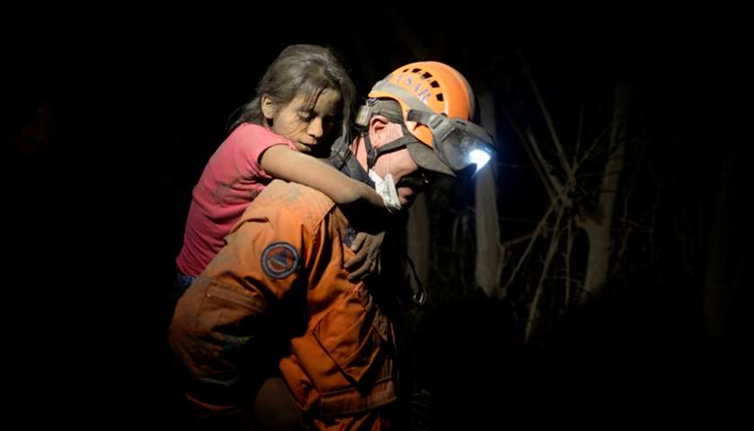 A rescue worker carries a child covered with ash after Fuego volcano erupted