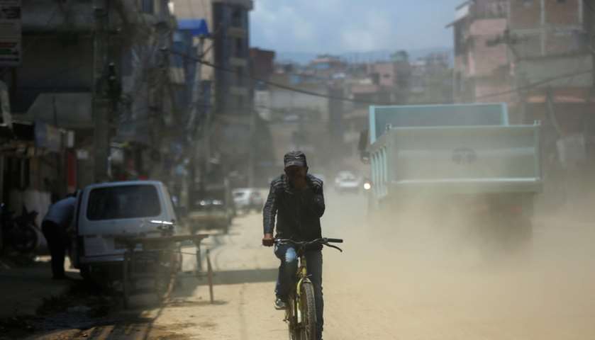 A cyclist covers his face as he rides along the dusty road - Kathmandu, Nepal