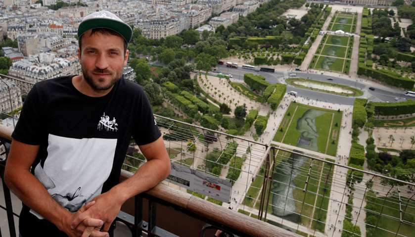 French  artist Saype poses at the Eiffel Tower in front of his giant artwork \"Beyond Walls\"