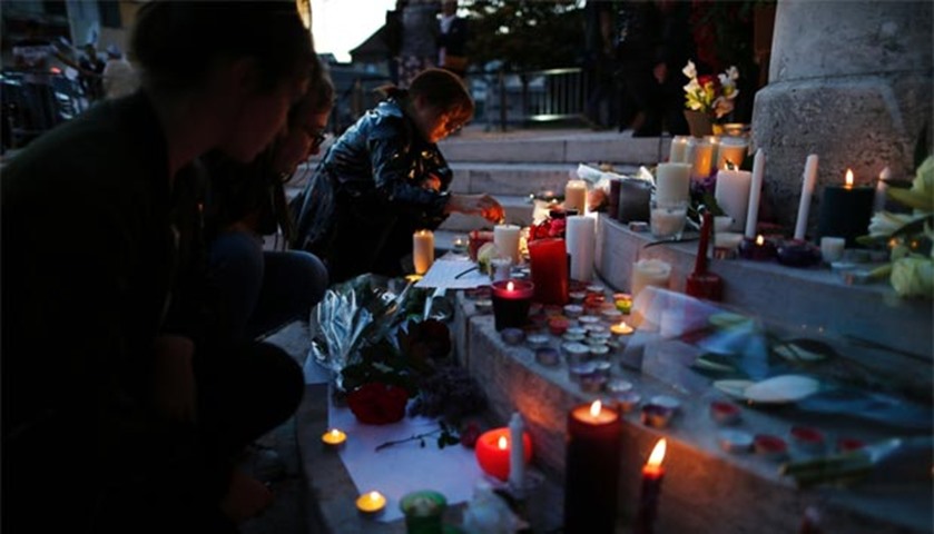 A woman lights a candle near a floral tribute in front of the city hall of Saint-Etienne du Rouvray