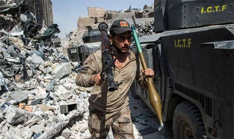 A member of the Iraqi forces walks through the rubble past humvees in the Old City of Mosul