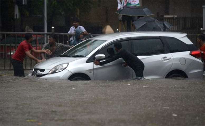 A stranded car is being pushed on a flooded street in Mumbai