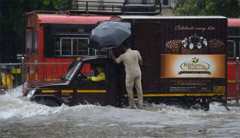 A man tries to drive a van along a flooded road in Mumbai