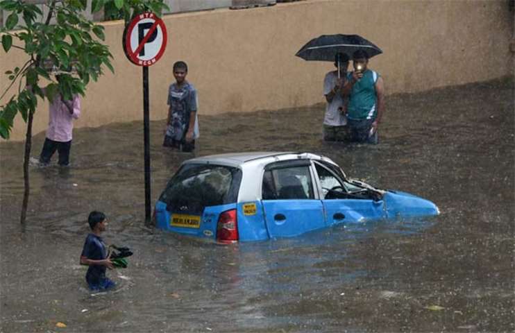 People gather around a submerged vehicle on a flooded street in Mumbai