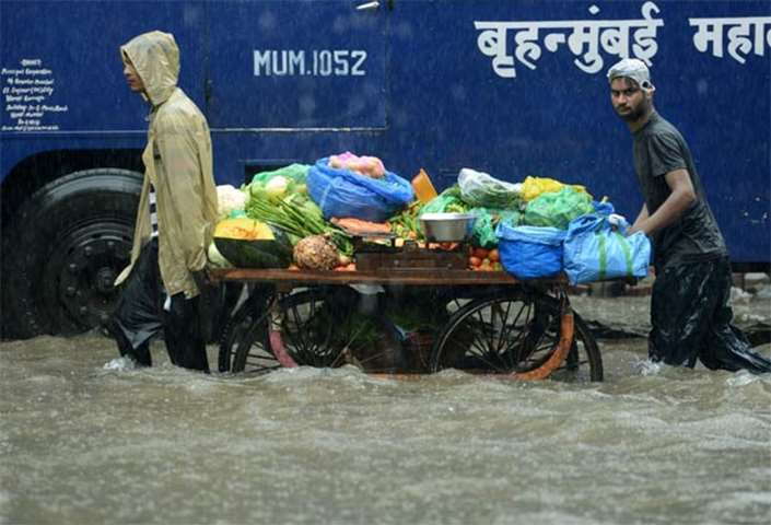 Vegetable vendors push their cart along a flooded street in Mumbai