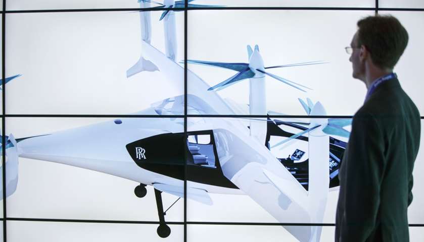 A man poses alongside screens presenting the Rolls-Royce EVTOL air taxi concept