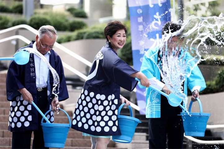 Tokyo Governor Yuriko Koike splashes water on the ground to cool down an area in Tokyo on Monday