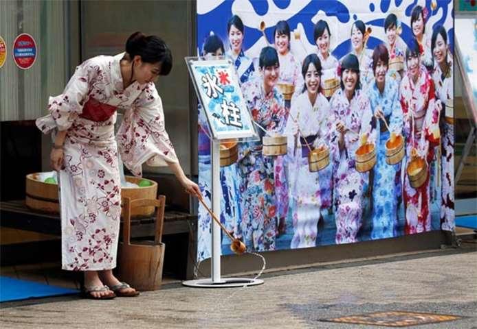 A woman wearing a Yukata, or summer kimono, splashes water onto the hot asphalt in Tokyo