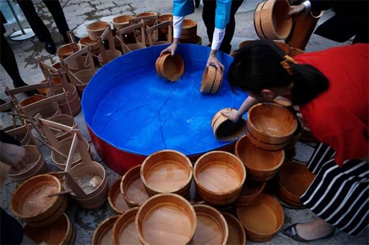 People fill wooden buckets with water during a water sprinkling event in Tokyo