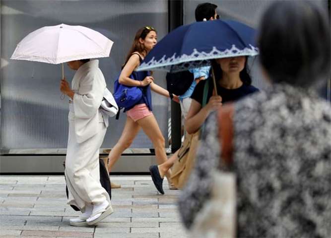 A kimono-clad woman using a sun umbrella walks on a street during a heatwave in Tokyo