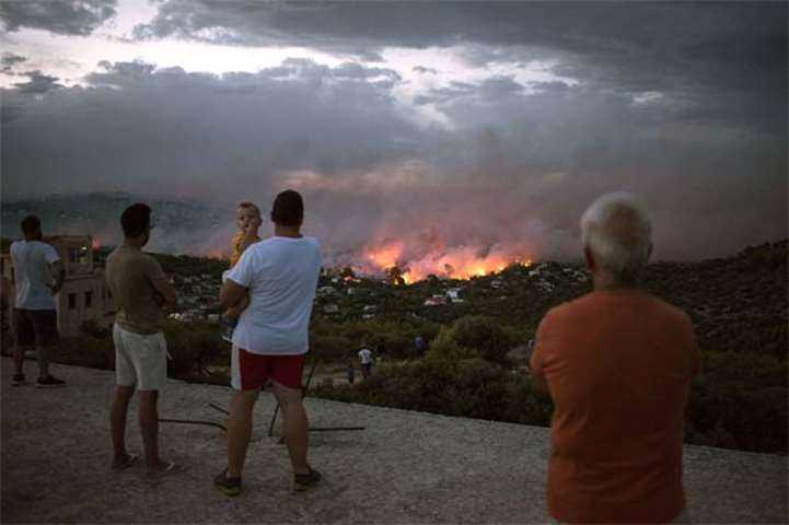 People watch as a wildfire burns in Rafina, near Athens