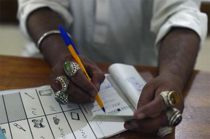 An election official notes down information of a voter at a polling station in Lahore