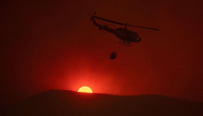 A helicopter carries water as the sun sets in the background while fighting the fire in Lakeport, Ca