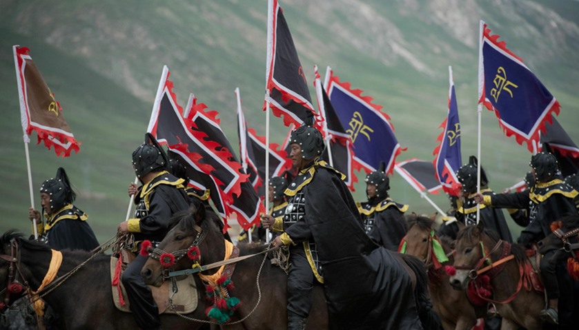 Ethnic Tibetans in traditional dress ride horses whilst holding flags