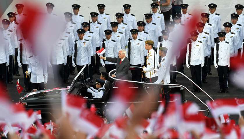 Singapore\'s President Tony Tan (C, in red tie) waves his country\'s flag during a drive past