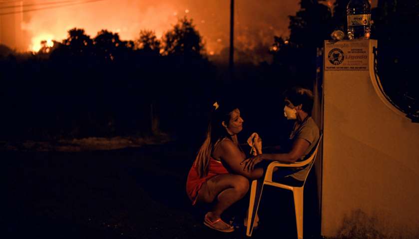 A woman tries to calm her neighbor as wildfire approaches the village