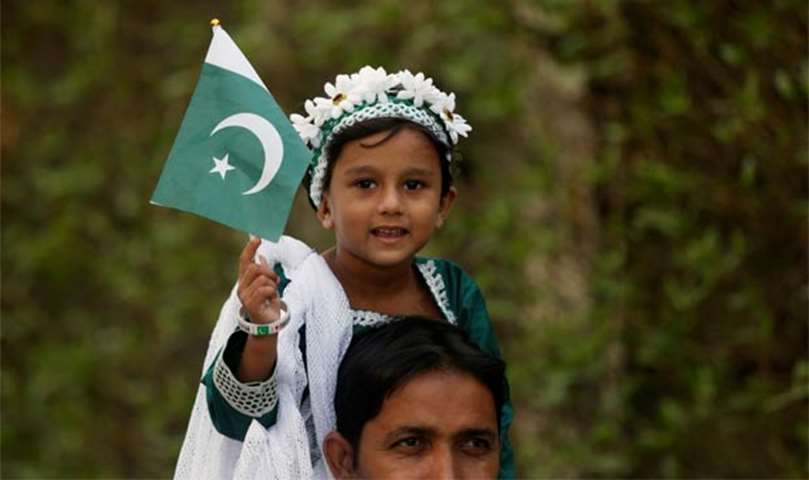 A girl holds a national flag as she sits on the shoulder of her father during a ceremony in Karachi