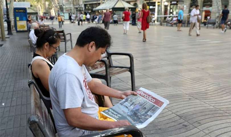 A man sits on a bench as he reads a newspaper at Las Ramblas street where a van hit pedestrians
