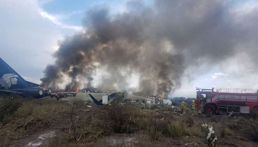 Firefighters douse a fire as smoke billows above the site where an Aeromexico-operated Embraer passe