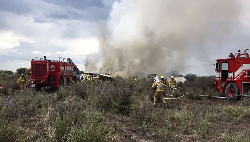 Durango\'s Civil Protection showing firemen working as smoke billows from the wreckage of the plane