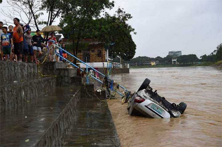 Residents look at a vehicle washed up on a swollen river after a heavy downpour in Manila on Sunday