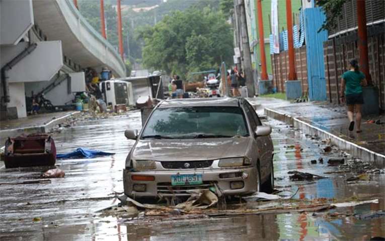 A resident walks past washed up vehicles on a road after flooding submerged homes in Marikina City