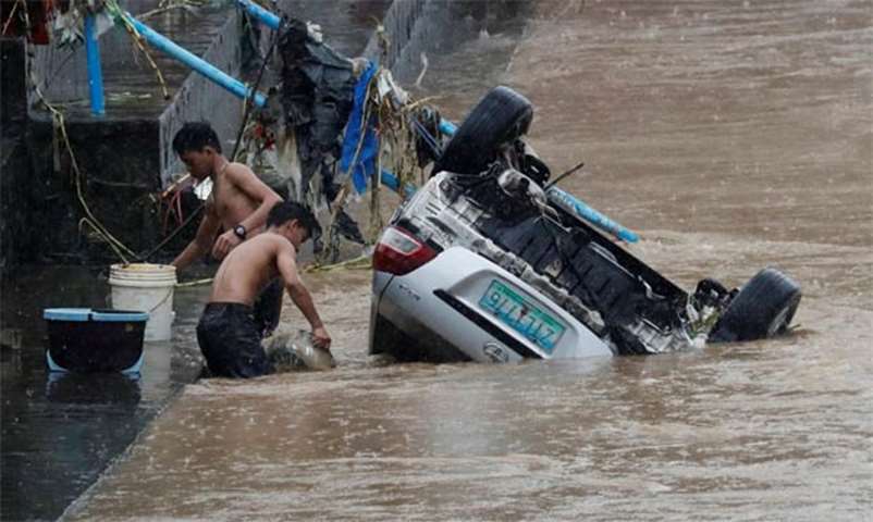 Residents fetch water next to a submerged vehicle swept by flash floods in Marikina
