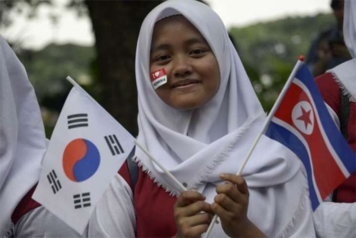 An Indonesian student holds a North Korea and a South Korea flag during the torch relay