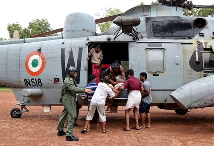 People help a woman disembark from an Indian Navy helicopter at a relief camp