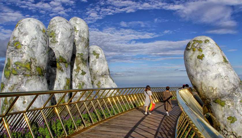 Tourists walk past giant hand structure on Gold Bridge on Ba Na hill near Danang city, Vietnam