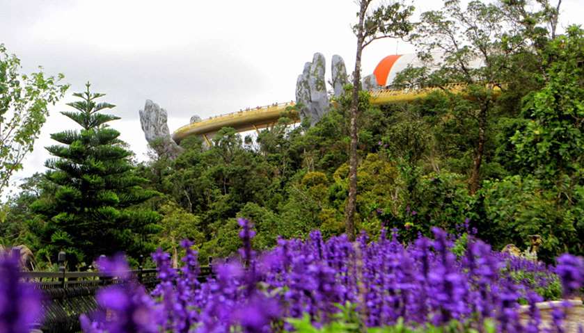 The 150-meter long Cau Vang \"Golden Bridge\" is seen past flowers and trees in the Ba Na Hills near D