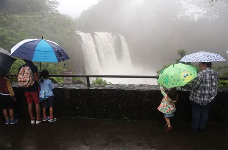 People gather to view Rainbow Falls, swollen from Tropical Storm Lane rainfall, on the Big Island