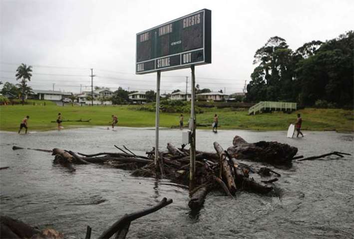 Floodwaters flow beneath a baseball scoreboard as residents bodyboard nearby on the Big Island