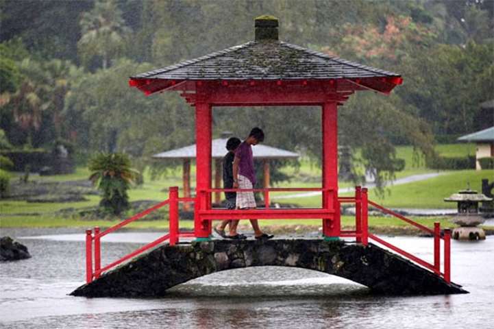 Two men walk through a park flooded by rain from Hurricane Lane in Hilo, Hawaii