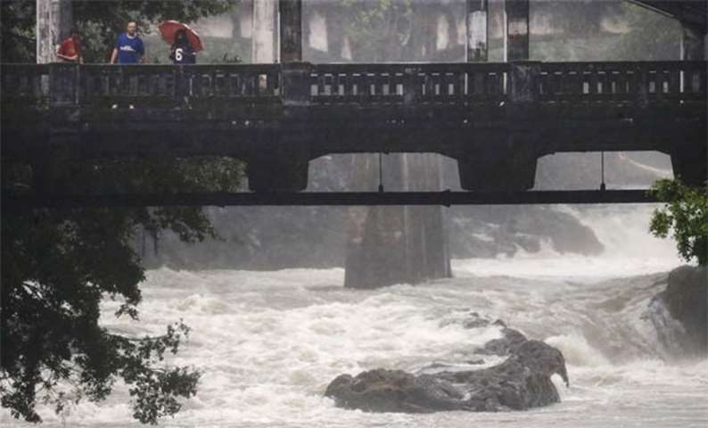 People stand on a bridge over the swollen Wailuku River during Tropical Storm Lane