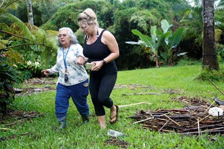 Jillane Bosscher helps her landlord Margaret Almada Collins walk through flood debris in Hilo