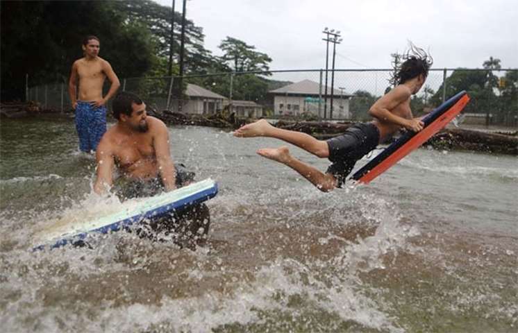 Residents play in floodwaters at a baseball field during flooding from Tropical Storm Lane in Hilo