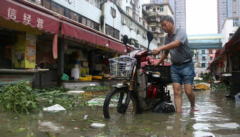 A man pushes a motorbike through a flooded street in Xiamen