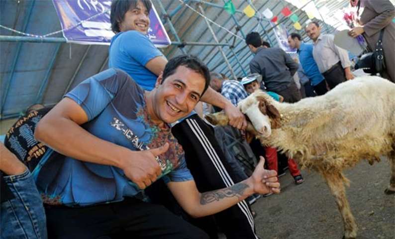 An Iranian man poses with a thumbs-up gesture as another holds the leg of a sheep in Tehran