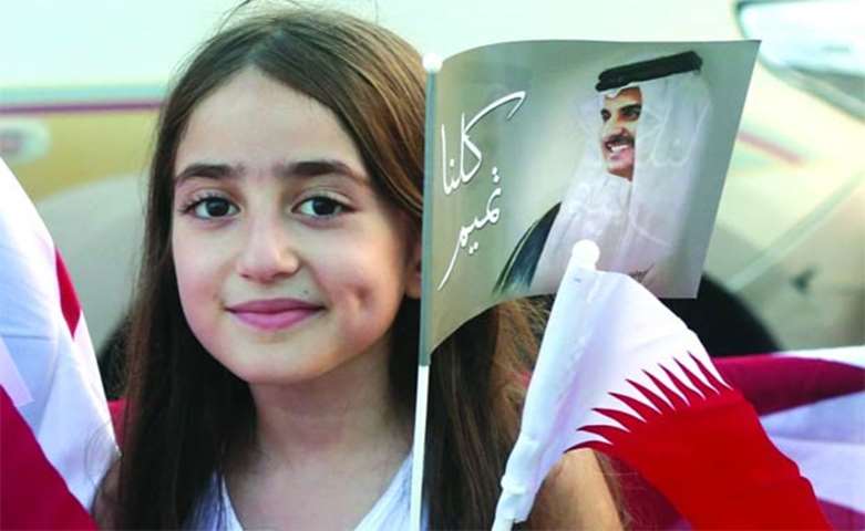 A young girl is seen carrying a portrait of the Emir and the Qatari flag