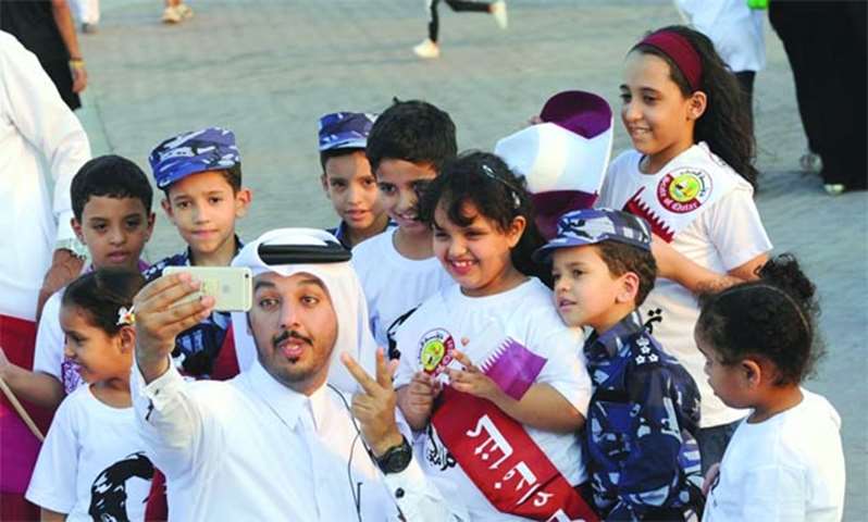 A citizen takes a selfie with children while waiting to greet His Highness the Emir