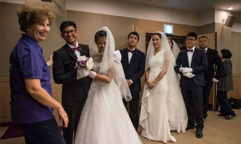 Wedding couples queue to pose for photos at a hotel before taking part in the ceremony