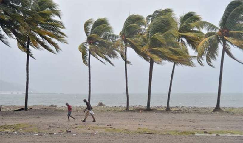 Haitian people walk through the wind and rain on a beach in Cap-Haitien