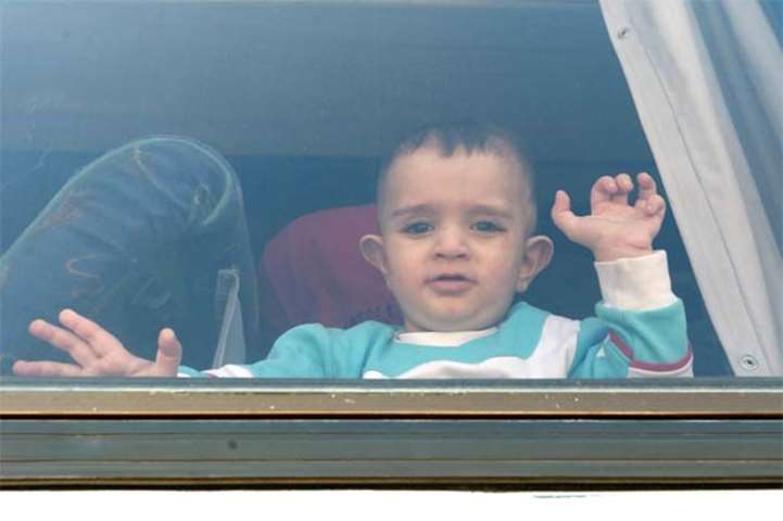 A Syrian toddler waves through the window of a bus as refugees leave the Lebanese capital