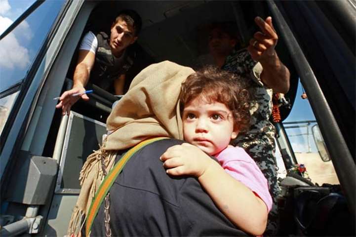 A Syrian woman steps into a bus with a child in her arms as refugees leave Beirut on Sunday