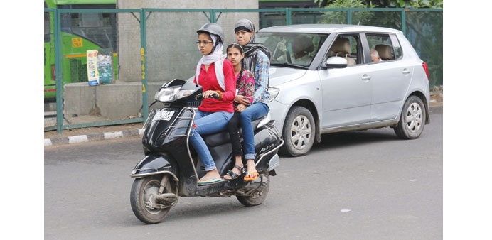 A helmeted woman rides her moped carrying two friends without helmets in New Delhi yesterday.