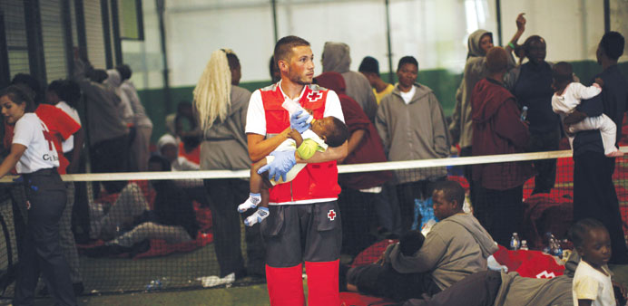 A member of Spanish Red Cross feeds an African immigrantu2019s baby next to other illegal immigrants at a sports centre in the southern Spanish port city 