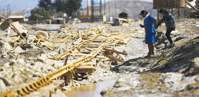 Locals walk next to a damaged railway line after a flood at Diego de Almagro town.